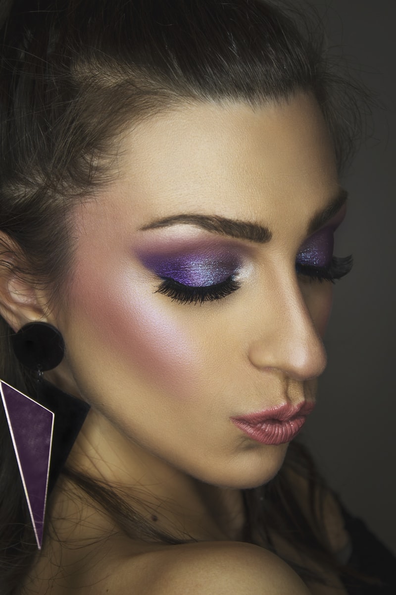 Model with shimmering violet editorial eye makeup and sculpted cheekbones, eyes closed