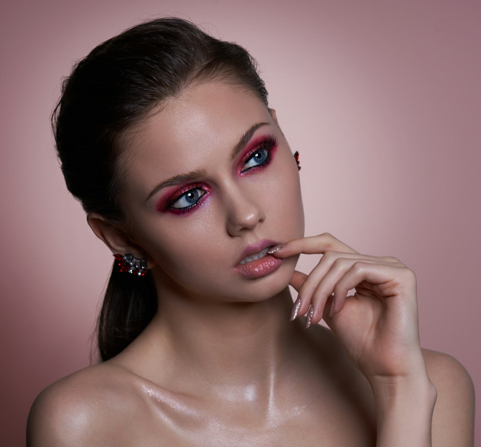 Model with rose-toned editorial eye makeup and glossy lips against a blush backdrop