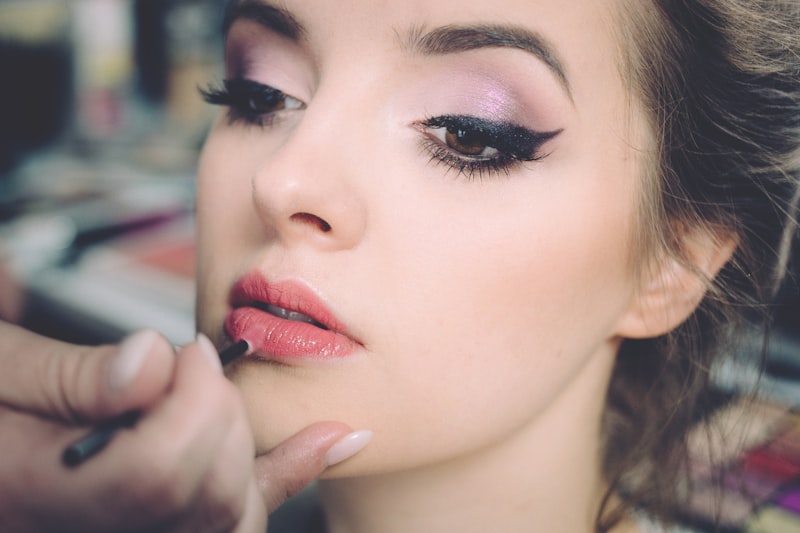 Makeup artist applying rose lip color to a client with a winged liner and soft lilac eye
